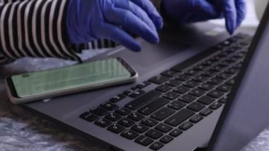 Masada eldivenlerle çalışan genç bir bayanın fotoğrafını çek. Karantina, kendini izole etme. Kız dizüstü bilgisayara bak. Serbest yazar, uzak çalışma, evde çalışma, uzaktan öğrenme..