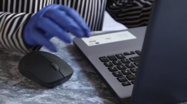 Masada eldivenlerle çalışan genç bir bayanın fotoğrafını çek. Karantina, kendini izole etme. Kız dizüstü bilgisayara bak. Serbest yazar, uzak çalışma, evde çalışma, uzaktan öğrenme..