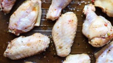 Kızartmadan önce tavada çiğ tavuk teriyaki kanadı. Fırın tepsisinde birkaç çiğ tavuk kanadı. Yağ içinde tavuk eti ve siyah tavada baharat, pişirme süreci.