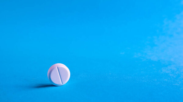 Белые круглые медицинские таблетки на синем фоне. Распространенные белые таблетки на столе. Понятие медицины, фармацевтики и здравоохранения. Свободное место для текста или логотипа
