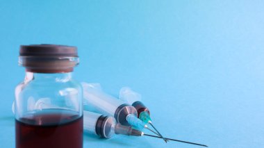 Mavi arka planda kırmızı iksirli bir tıbbi cam şişe ve üç tane de tek kullanımlık şırınga. Tıbbi konsept bir tıbbi test tüpü ve koronavirüse karşı aşılar gösteriyor. Yer kopyala.