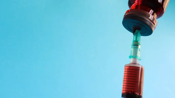 一支注射器从一个红色的液体瓶中伸出来 被蓝色的背景隔离了药品 疫苗和一次性注射器 药物概念 无菌瓶玻璃安培注射器 — 图库照片