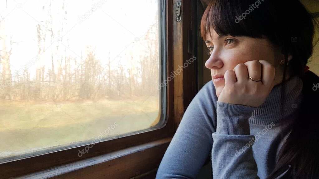 Young pretty woman traveling on a classic train sitting near the window. vintage filter. Girl tourist looks out the window of a moving old train, enjoying travel and natural beautiful scenery