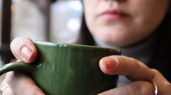 La chica bebe una bebida caliente por la mañana. Una mujer sostiene una taza de té o café cerca de sus labios. Taza verde cerámica reutilizable con cacao o leche caliente . —  Fotos de Stock