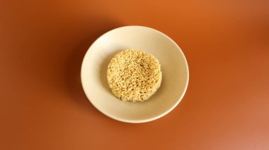 Kahverengi arka planda, seramik bej bir çorba kasesinde çiğ hazır şehriye. Makarna, hazırlamak için kaynar su dökmeye ve birkaç dakika beklemeye yeter. Boşluğu kopyala.