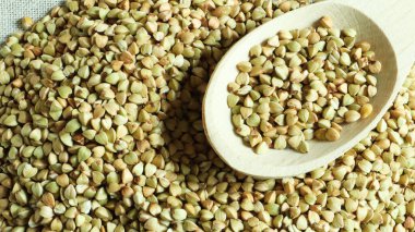 Karabuğday arka planda dağınık, tahta kaşıkta çiğ yeşil mısır gevreği. Sağlıklı Groats. Kızartılmamış organik vejetaryen yiyecekler. Sağlıklı ve dengeli beslenme kavramı. Diyet ürünü. Sağlıklı gıdalar