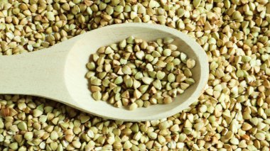 Karabuğday arka planda dağınık, tahta kaşıkta çiğ yeşil mısır gevreği. Sağlıklı Groats. Kızartılmamış organik vejetaryen yiyecekler. Sağlıklı ve dengeli beslenme kavramı. Diyet ürünü. Sağlıklı gıdalar