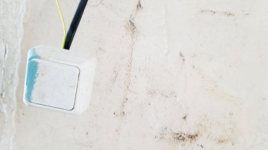 Boya ve macundaki bir beyaz ışık düğmesi, bitmemiş bir duvarın arka planında tamir sırasında geçici olarak siyah bir kabloya asılıyor. Kabloları aç.