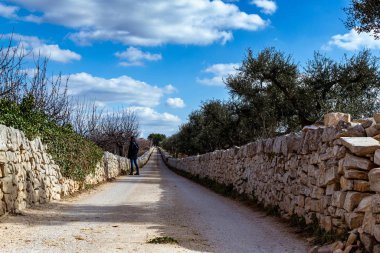 Bulutların altında kuru taş duvarlar olan kırsalda bir cadde.
