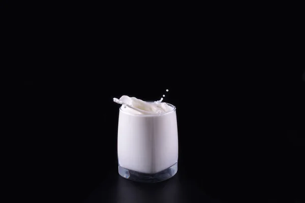 glass of milk and milk splashes, black background, side view