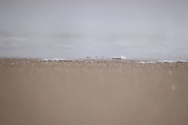 Close up of white bubbles on water surface from beach with blur sandy background — 스톡 사진