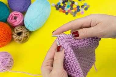 Kız sarı arka planda bir çocuk eşarbı örüyor.