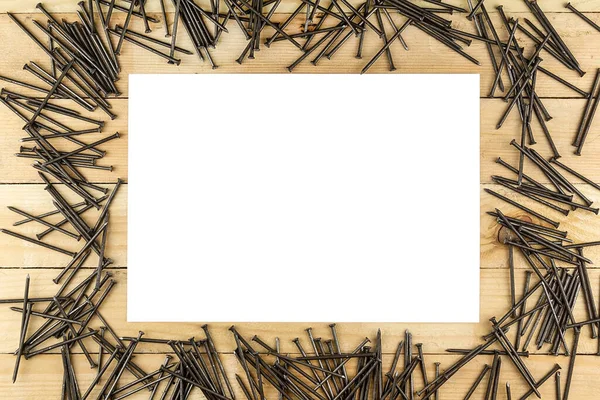 metal nails are scattered on the wooden surface, next to a sheet of white paper.fasteners on a wooden background