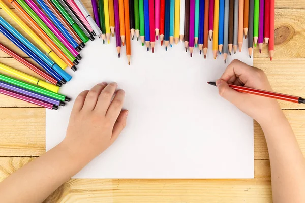 the child draws and a lot of pencils and paints for drawing on a wooden background