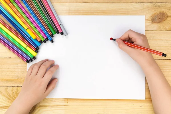 the child draws and a lot of pencils and paints for drawing on a wooden background