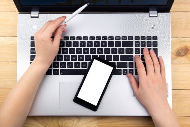 Kız dizüstü bilgisayarda çalışıyor, elinde bir kalem tutuyor ve grafiği işaret ediyor. Klavyede bir akıllı telefon var.