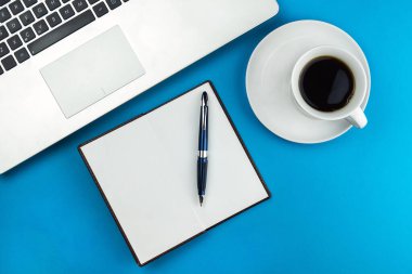 dizüstü bilgisayar, kahve fincanı ve mavi arka planda bir kalem..