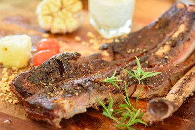 Sarımsak, domates ve yeşil sebzelerle süslenmiş ahşap bir tabakta pişmiş domuz pirzolası.