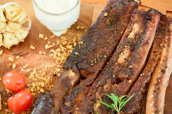 Sarımsak, domates ve yeşil sebzelerle süslenmiş ahşap bir tabakta pişmiş domuz pirzolası.