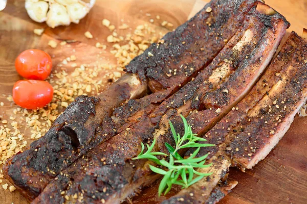 Sarımsak, domates ve yeşil sebzelerle süslenmiş ahşap bir tabakta pişmiş domuz pirzolası.