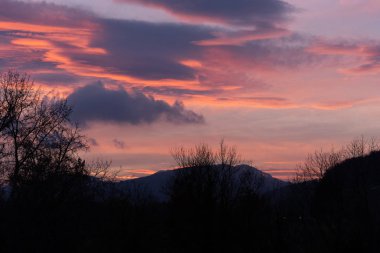 Dramatic sunset with pink clouds over bar trees and hills in wintertime in Switzerland. Unprocessed and original.