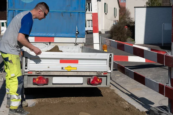 Joven técnico de tuberías en obra cierra portón trasero de un remolque cargado de arena . — Foto de Stock