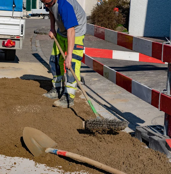 Trabajador de construcción con gafas de sol y escoba limpiando arena en obra . — Foto de Stock