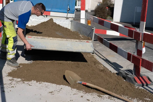 Joven técnico de tuberías en obra cierra portón trasero de un remolque cargado de arena . — Foto de Stock