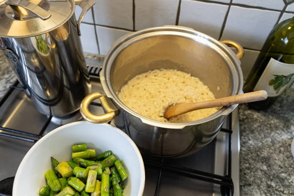 Kuşkonmaz, soğan ve beyaz şarapla Risotto pilavı pişiriyorum. Tavanın önünde pirinçle dilimlenmiş kuşkonmaz. Yüksek açı görünümü.