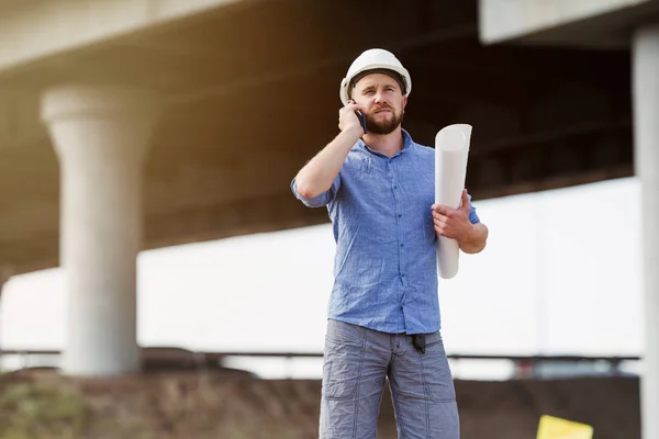 身穿白色防护头盔的准将在建造中的大桥跨度的背景下与建筑师通电话 — 图库照片
