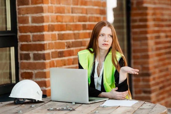 一个红头发的建筑师女孩穿着一件黄色背心坐在办公室里 满脸不悦地看着别处 — 图库照片