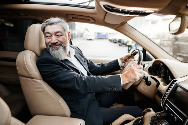 The white haired driver of the Executive car with a smile turns to the back seat and talks to the passenger