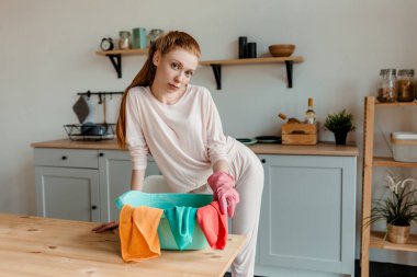 Kızıl saçlı kız, sarı eldivenli hizmetçi ev temizliğine hazırlanıyor.