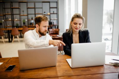 Ofiste oturan sakallı bir erkek yönetici şirketin yeni bir çalışanını eğitiyor.
