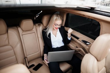 Bir iş kadını kucağında dizüstü bilgisayarla birinci sınıf bir yönetici arabasının arka koltuğunda oturuyor ve başarılı bir iş sözleşmesi imzalamaktan mutluluk duyuyor.