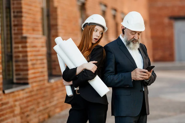 一位红头发的女建筑师正在偷看一位年迈的灰发工程师的电话 — 图库照片