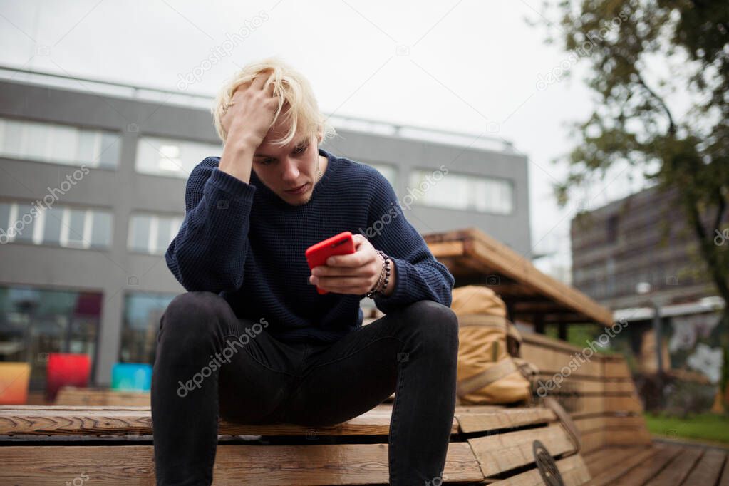 A young guy is sitting in a Park, holding his head in confusion, because he was abandoned by a girl online by correspondence in a chat