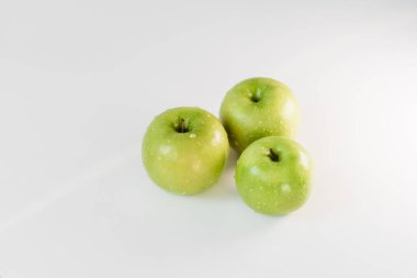 Fresh green apples with water droplets on a white glossy kitchen table. Tasty bright juicy fruits. Healthy eating. Isolated object.