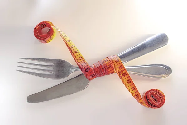 Χάνω βάρος. Ένα πιρούνι και μαχαίρι είναι τυλιγμένα σε μια κόκκινη ταινία μέτρησης σε λευκό φόντο — Φωτογραφία Αρχείου