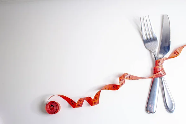 Χάσε βάρος. Ένα πιρούνι και μαχαίρι είναι τυλιγμένα σε μια κόκκινη ταινία μέτρησης σε λευκό φόντο στα δεξιά — Φωτογραφία Αρχείου