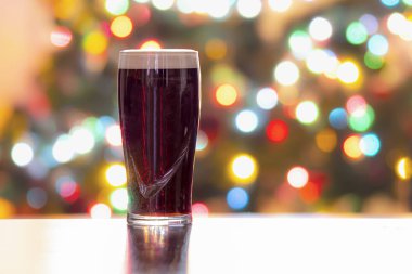 Arka planda Noel ışıkları olan bir bira. Guinness koyu İrlanda likörü. Yatay Görünüm
