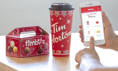 Calgary, Alberta. Kanada 28 Aralık 2019. Noel 'de Tim Hortons uygulamasını kahve ve bir kutu Tim Bits ile kullanan biri. Tim Hortons başkanı Alex Macedo Mart 'ta ayrılıyor.