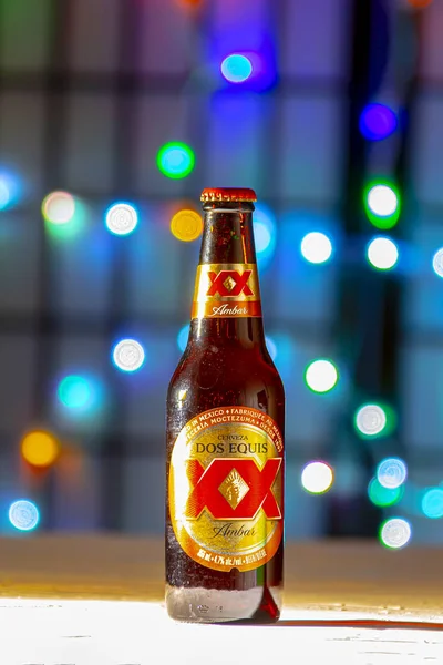 Hnědá láhev dos equis Beer. Mexické pivo na bílém povrchu textury na barevných rozostřených světlech — Stock fotografie