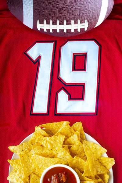 An American football with organic nacho chips and mild salsa on a white red football jersey with the 19 number — ストック写真