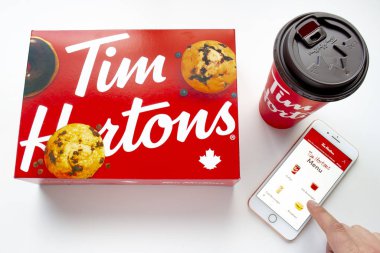 Calgary, Alberta. Kanada 27 Ocak 2020. Bir kişi iPhone kullanıyor. Ayrıca Tim Hortons uygulamasını kullanıyor. Beyaz arka planda kahve ve bir kutu donut var.