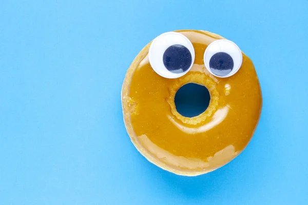 Kanadský javor Dip kobliha s černými kroutit googly oči na modrém pozadí — Stock fotografie