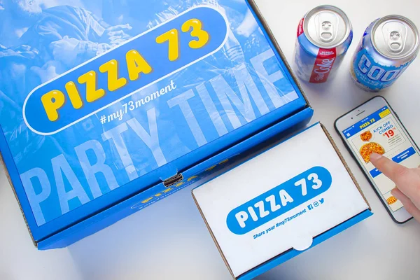 Uma caixa de pizza 73 Pizza com asas e uma Coca-Cola Dieta com Nestea pop e pessoa usando o aplicativo Pizza 73 — Fotografia de Stock