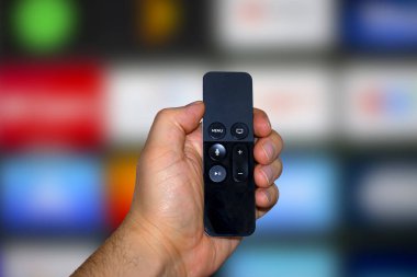 Arka planda televizyon ekranı olan dijital ortam oynatıcı ve mikro konsol kumandası tutan bir kişi