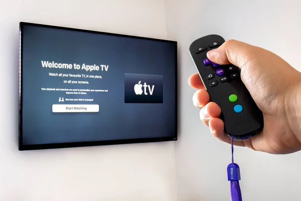 stock image Calgary Alberta, Canada. May 5, 2020. A person holding a Roku remote control with the apple tv application open a screen tv on the background