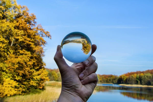 hand, reflection in the glass ball, forest and lake in autumn